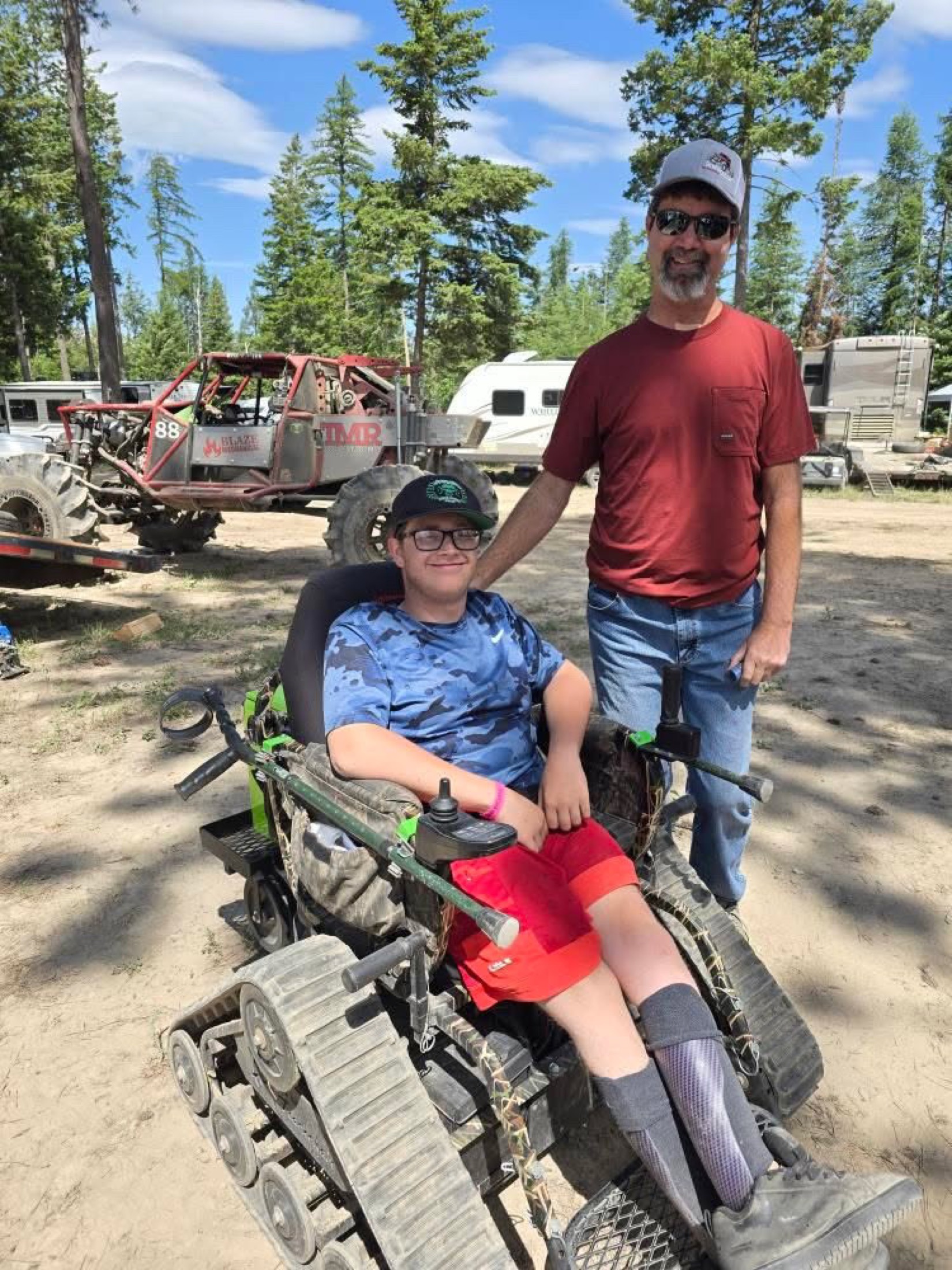 Brent standing beside a young person using an all-terrain mobility chair
